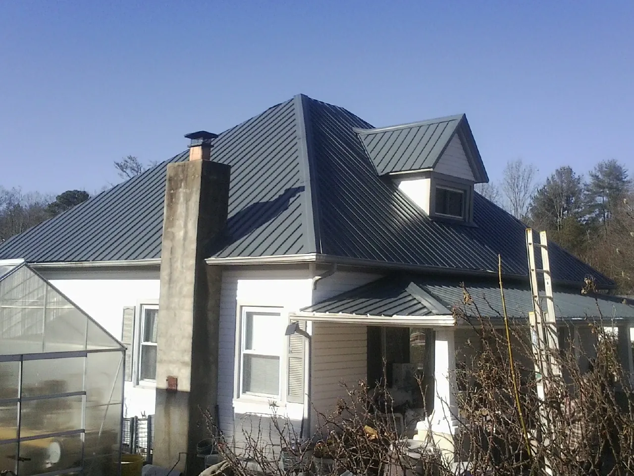 Dark blue standing seam metal roof on a white farmhouse with dormer — Slate & Tile Roof Repair by Roofing Brothers in Erskine