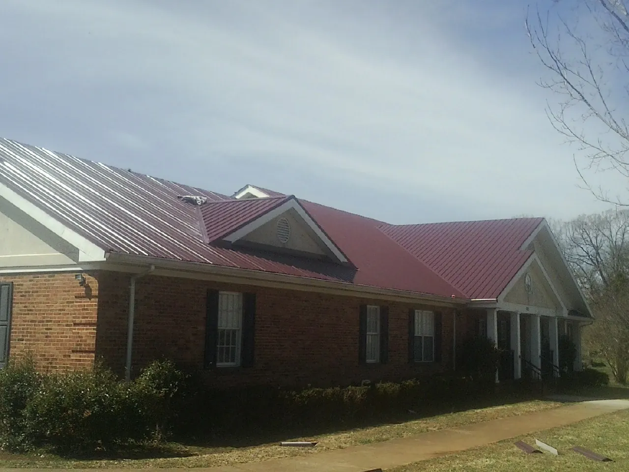Red metal roof with gabled entries on a long brick building, from a Hail Damage Roof Repair job in Erskine
