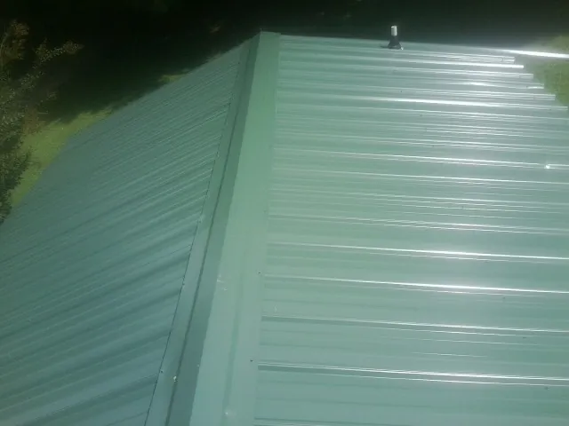 New green metal panels meeting at the ridge of a roof — Flat Roof Repair work by our crew in Erskine