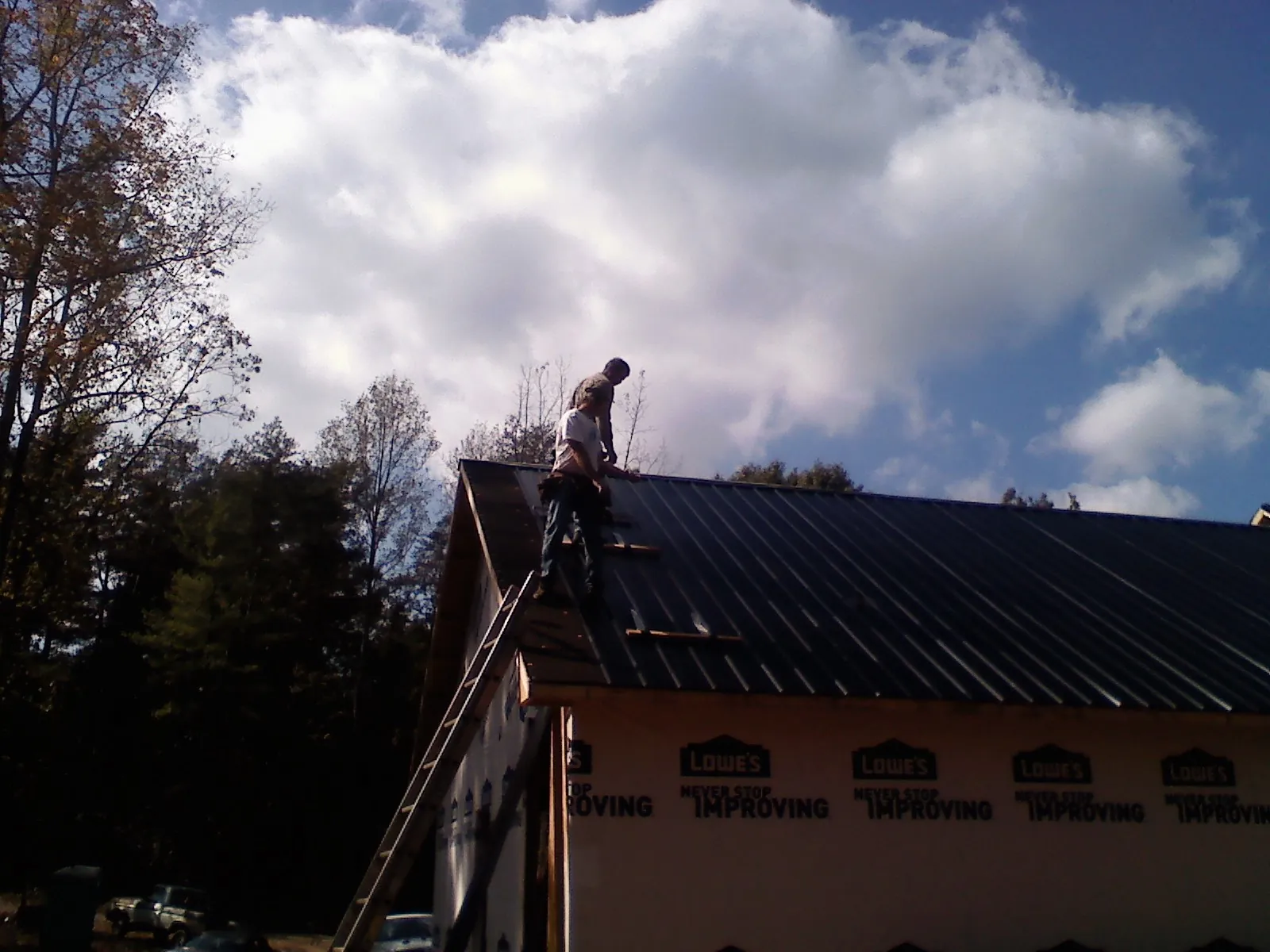 Roofer fastening dark metal panels high against a cloudy sky, from a Roof Inspection job in Erskine