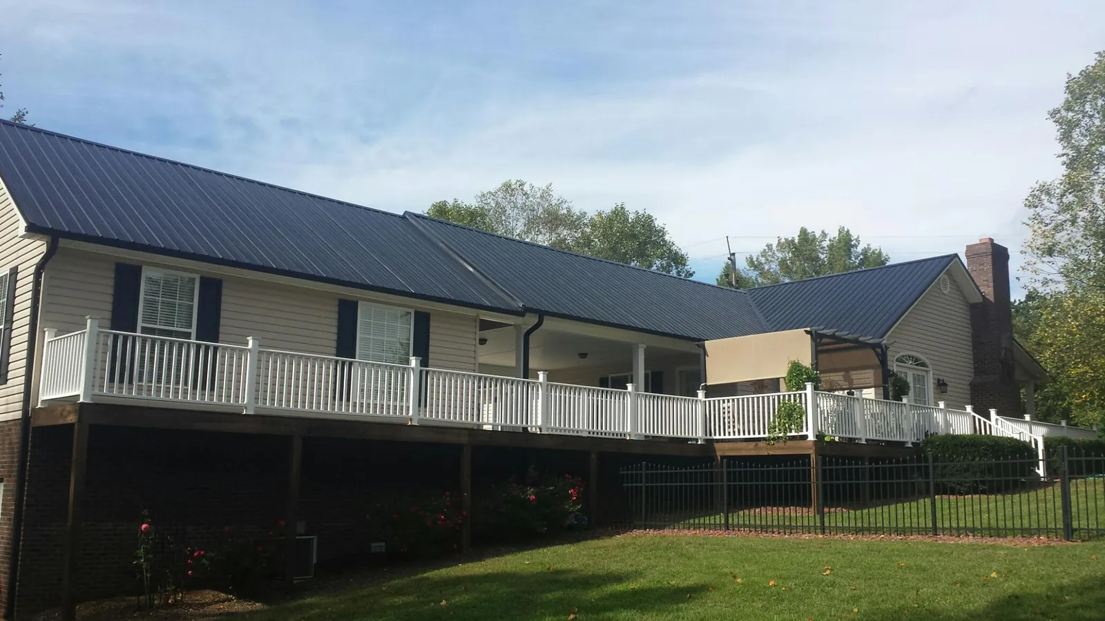 Black metal roof above a long white railed deck on a hillside home in Erskine