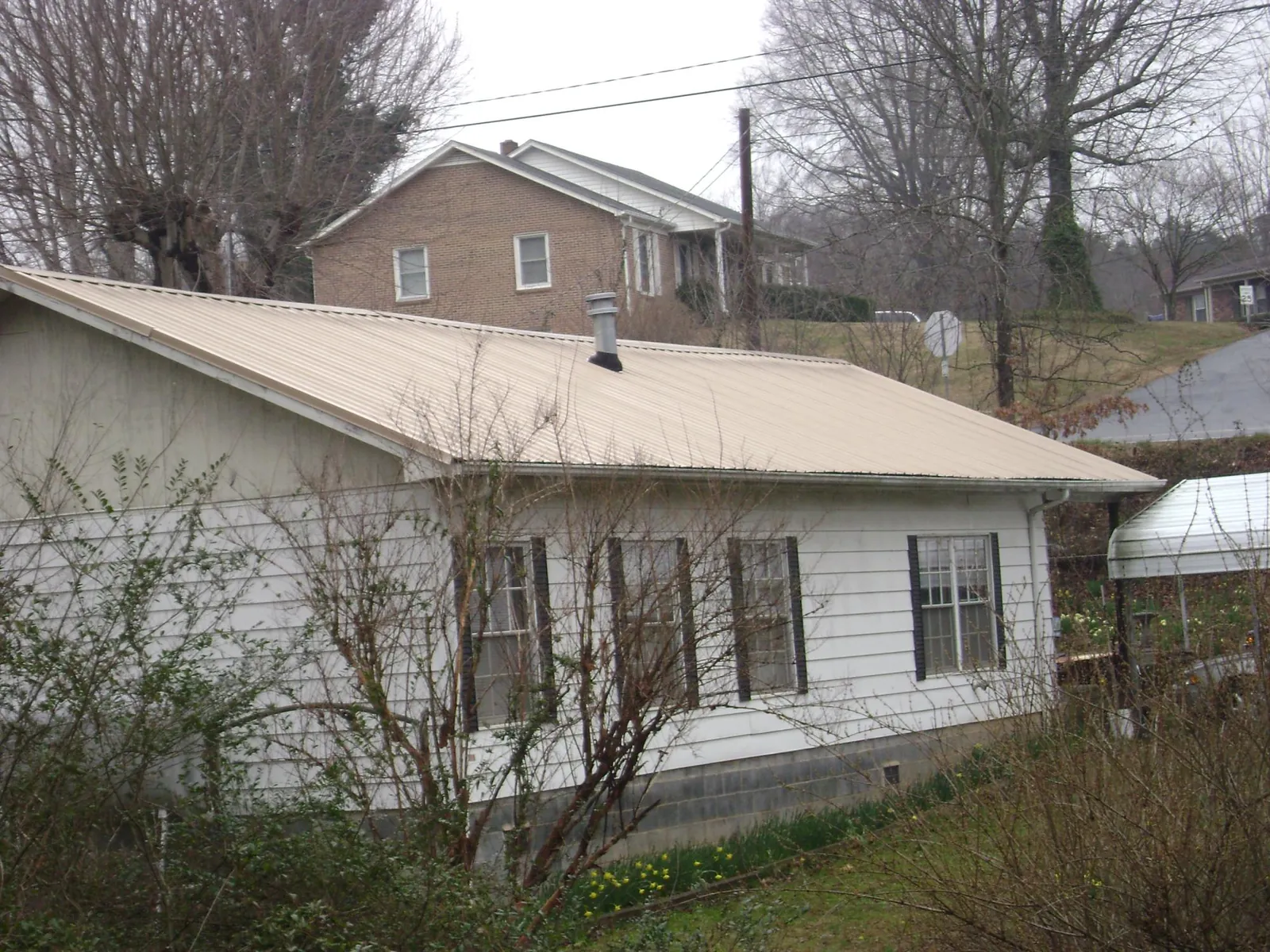 Tan metal roof on a white sided house set into a hillside — Commercial Roofing by Roofing Brothers in Erskine